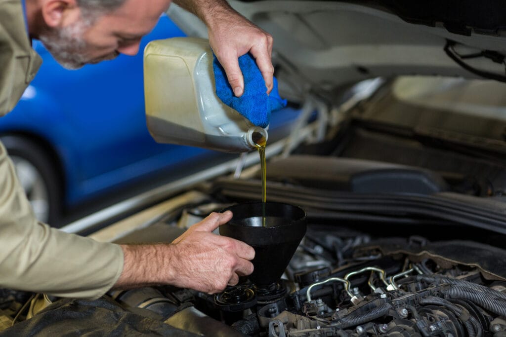 Mechanic pouring oil into car engine in repair garage
